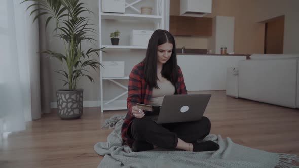 Beautiful Young Woman with Laptop and Bank Card Makes Online Shopping at Home