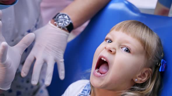 Little child in stomatology chair opens her mouth wide and shows her teeth to the doctor