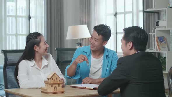 Couple Receiving The Keys From A Real Estate Agent After Signing On House Purchase Contract Paper