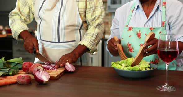 Senior man chopping vegetables while woman preparing salad in kitchen