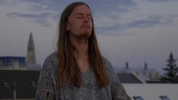 Young Man With Long Hair Meditating On City Roof