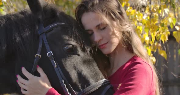 Close-up Portrait of a Young Caucasian Girl Caressing Horse Face in the Autumn Forest and Smiling