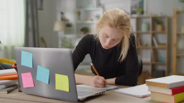 Young Beautiful Woman Studies at Home at a Desk