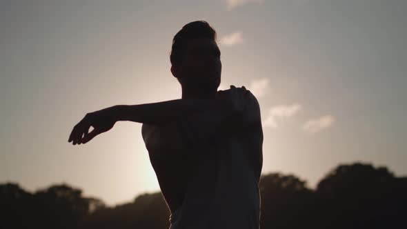 Man Stretches Before He Works Out Whilst Being Silhouetted By The Evening Sun In Slow Motion