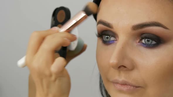 Makeup Artist Leads a Woman in the Face with a Brush for Applying Powder Foundation or Concealer