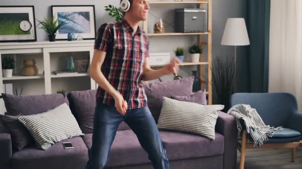 Funny Guy in Headphones Is Listening To Music, Dancing and Singing at Home Having Fun During Leisure