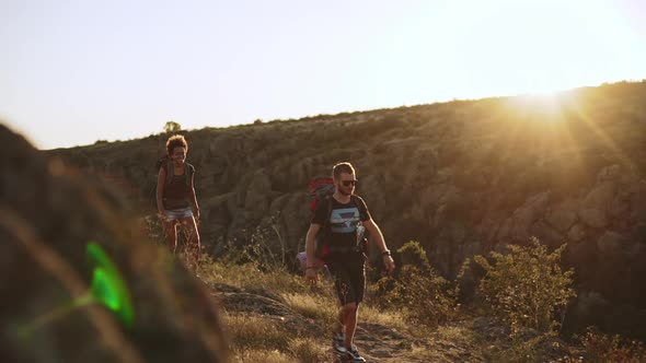 Bearded Male Wearing Backpack and Black Sunglasses with Two Females Walking Outdoors with Map in