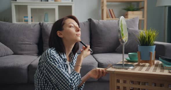 Beautiful Woman Putting on Make-up with Brush Looking at Mirror at Home