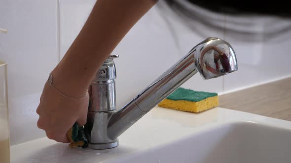 Woman cleaning the bathroom sink with a yellow sponge.