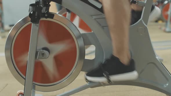 Side View of Male Feet in Sneakers Pedaling Cycling Equipment in Sports Club. Unrecognizable