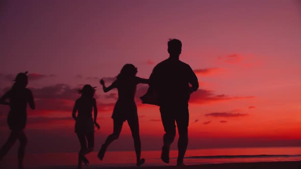 Back view silhouette. A group of young Asian friends having fun on the beach at sunset.