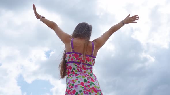 Girl with Raised Arms on the Background of the Sky