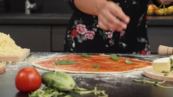 Female adding basil leaves to italian pizza margherita.