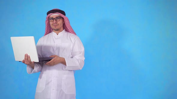 Arab Man on an Isolated Blue Background with Laptop Looking at Camera