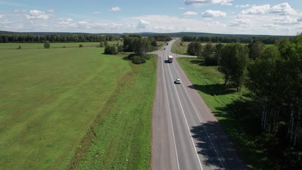 Aerial View of Scenic Road Between Green Trees with Pines on a Sunny Summer Morning