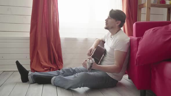 A Man Sits on the Floor Plays the Guitar at Home and Sings