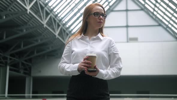 confident business woman with cup of coffee stands in lobby business center.