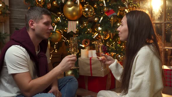 A Young Couple Sitting on the Sofa Near the Christmas Tree in Holding Glasses of Champagne