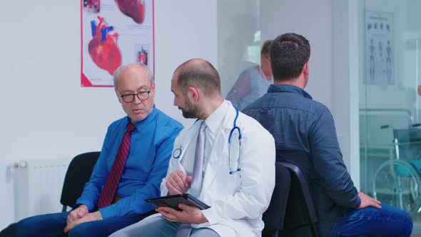 Doctor Discussing Diagnosis with Old Man in Hospital Waiting Area