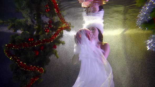 A Girl in a Christmas Dress, Which Flutters Tulle, She Is Under Water, Around Her Two Festive