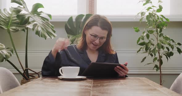 Mature Woman Having Breakfast at Table with Digital Tablet Read Good News