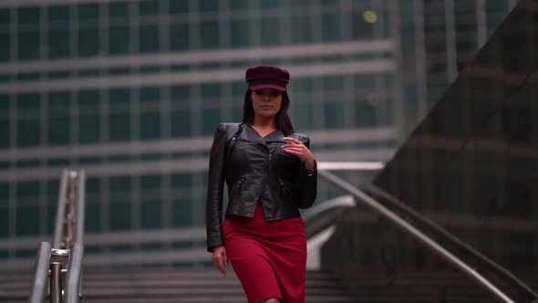 a Brunette with Long Hair in a Black Leather Jacket a Red Skirt and a Burgundy Cap Stands on the