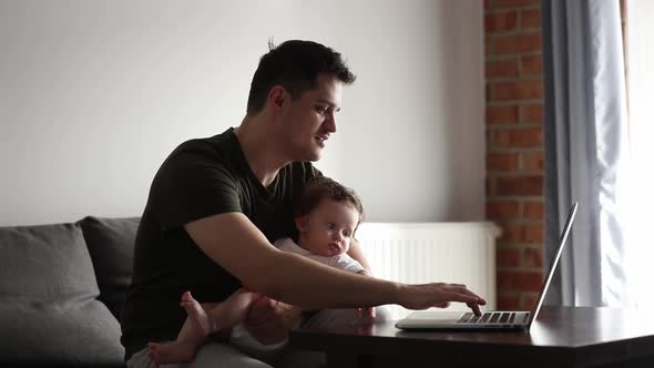 Father with infant child working on laptop computer at home