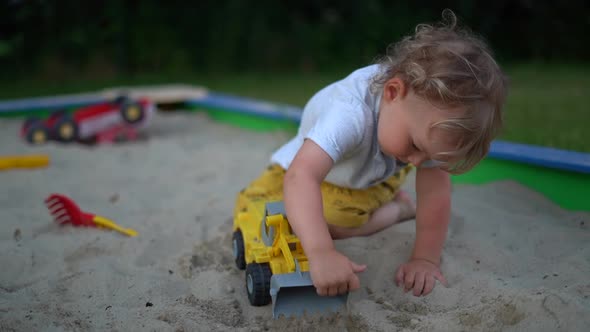 Little Boy Spends Time in a Sandbox and Holds a Plastic Dump Truck