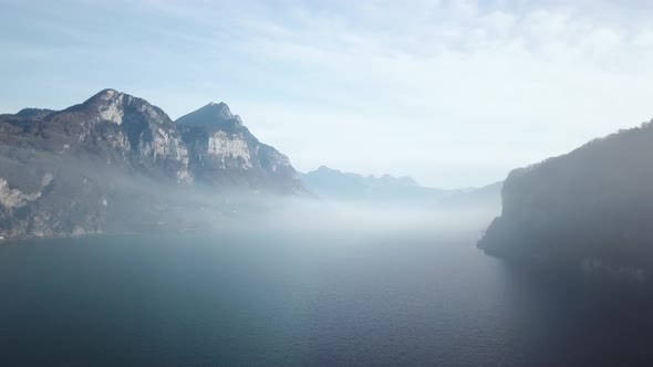Panoramic shot of low-hanging fog between mountain ranges above the water surface of a crystal blue