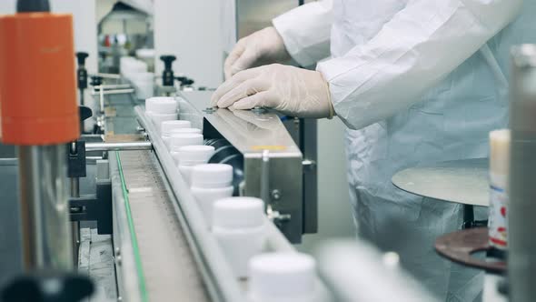 Factory Worker is Regulating a Conveyor with Pill Tubs