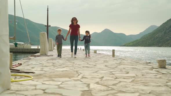 The Family Walks Along the Pier Against the Backdrop of the Sea and Mountains