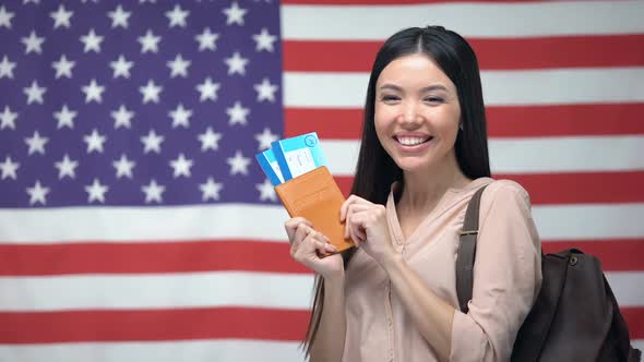Excited Woman Holding Passport and Flight Tickets Against USA Flag Background