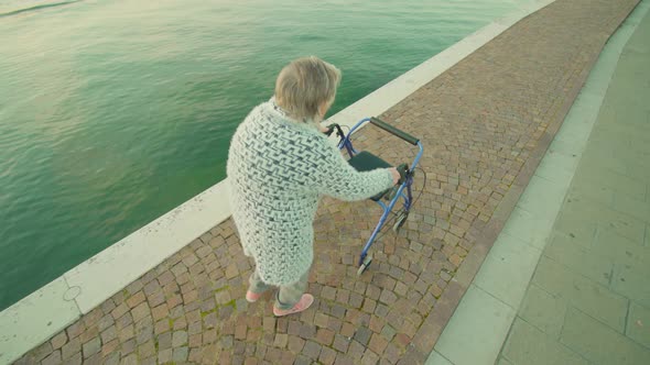 Old Lady Strolls Along Lagoon Bank with Wheelchairrollator