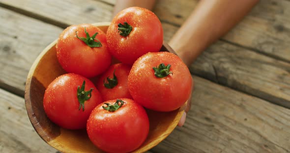 Video of biracial man holding bowl of fresh red tomatoes on wooden background