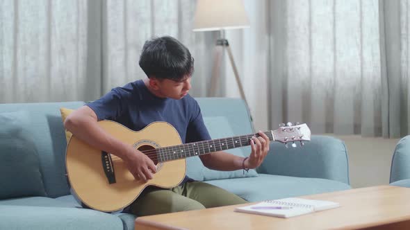 Asian Boy Composer With Note Book And Playing Guitar At Home