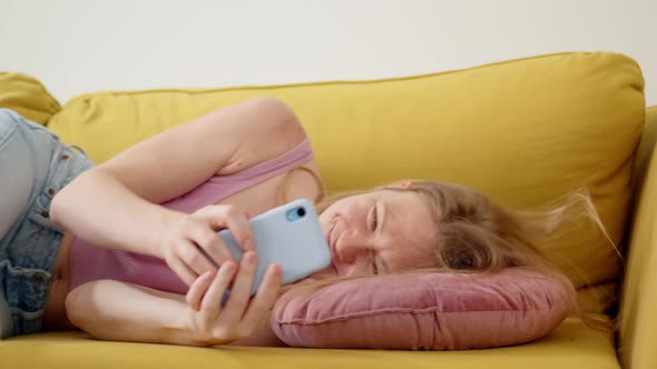 Happy and Cheerful Woman in Pink Tank Top Lies Down on Pillow on Yellow Sofa with Happy Expression