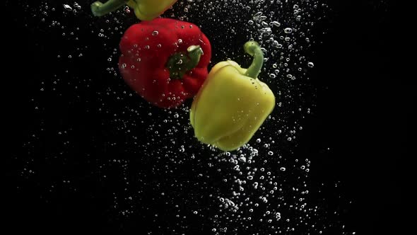 Red and Yellow Peppers Falling in Water and Spinning Air Bubbles on Black Background