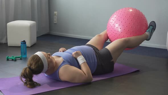 Obese Girl Trying to Train Lower Body Muscles Raising Big Gym Ball With Her Legs