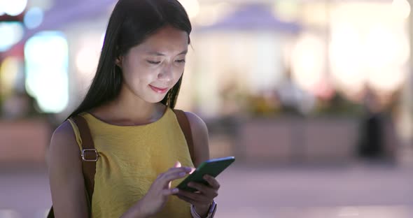 Woman sending audio message on cellphone in city of Shenzhen at night