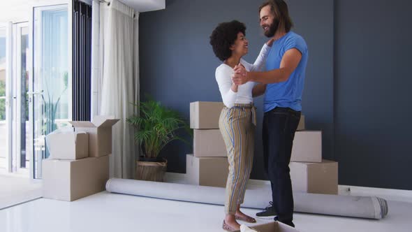 Mixed race couple dancing together in between cardboard boxes at new apartment house