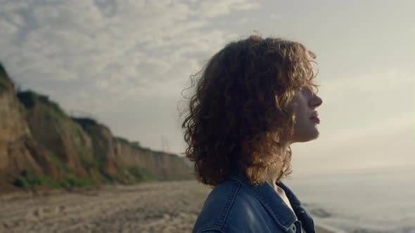 Curly Woman Looking Around Ocean Landscape at Sunrise