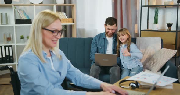 Disabled Woman Working on Laptop at Home and Waving Hands to Her Loving Caring Bearded Husband