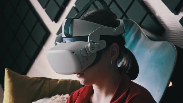 Young Woman in VR Helmet Sitting on Sofa and Communicating in Virtual World