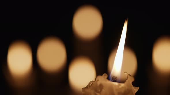 Wax Burning Candle Flickers in Dark on a Black Background with Blurred Candlelight Bokeh Effect