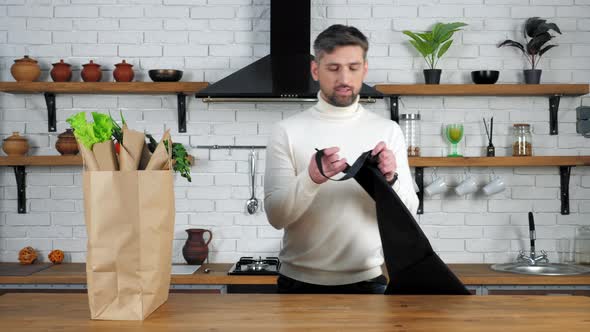 Man in sweater comes to home kitchen puts on apron preparing cook healthy food