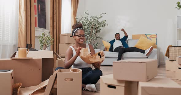 A Beautiful Woman Sits on the Floor of a Purchased Rented Apartment Unpacks Cardboard Moving Boxes