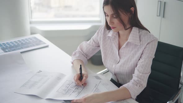 Attractive Girl Working with Documents Drawings Sitting at the Table in the Office