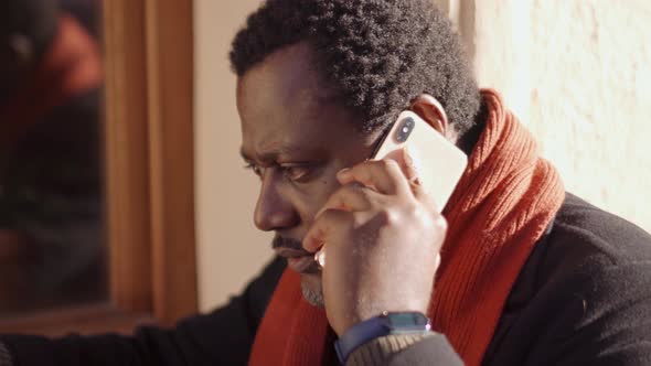 Pensive African man talking by phone in cafe