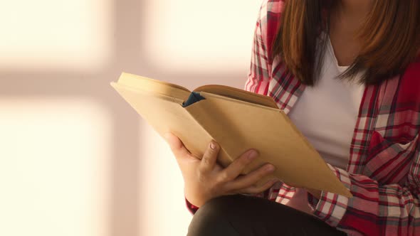 Unrecognizable Young Woman Reading A Paper Book Sitting Indoors Cropped