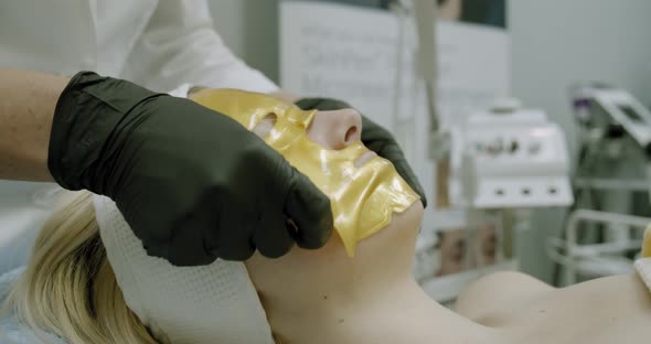 Cosmetologist Applying Gold Facial Mask To the Face Woman